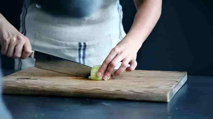 Someone chopping onions on a wooden cutting board