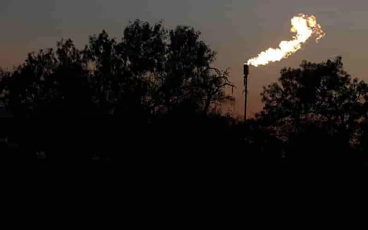 Gas well pressure relieve pipe with a big flame shooting up above the trees at night
